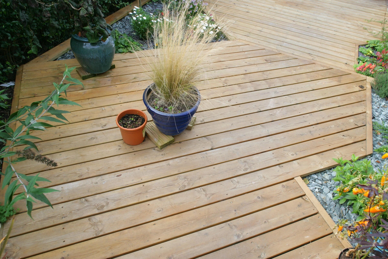 Decking in a garden with plant pots, shrubbery and grass and gravel surrounding it. Decking in a garden with plant pots, shrubbery and grass and gravel surrounding it.